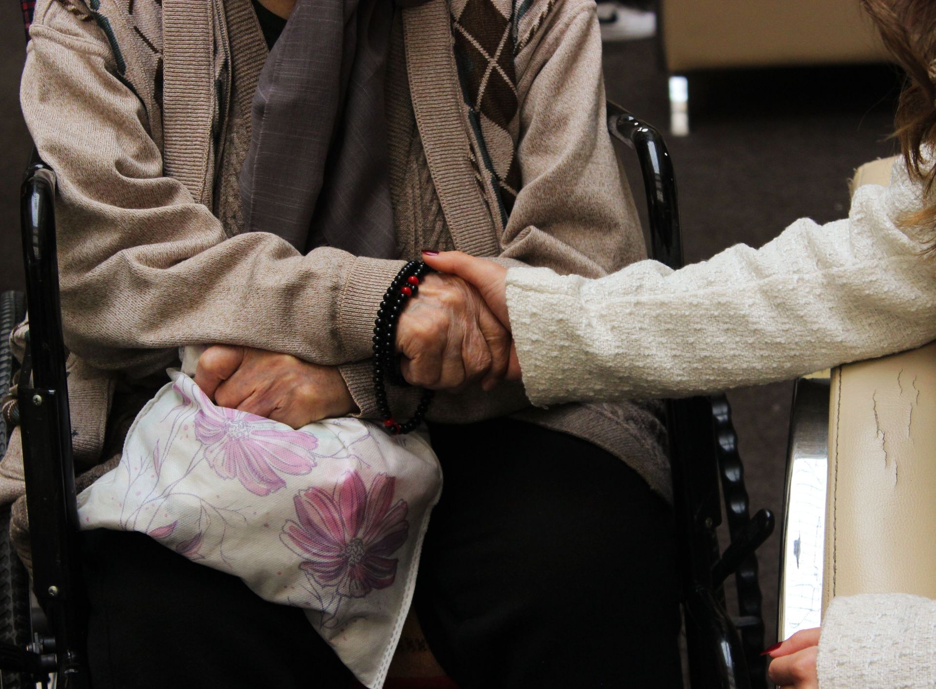 Elderly woman in wheelchair warmly holding another's hand, symbolizing care and support.